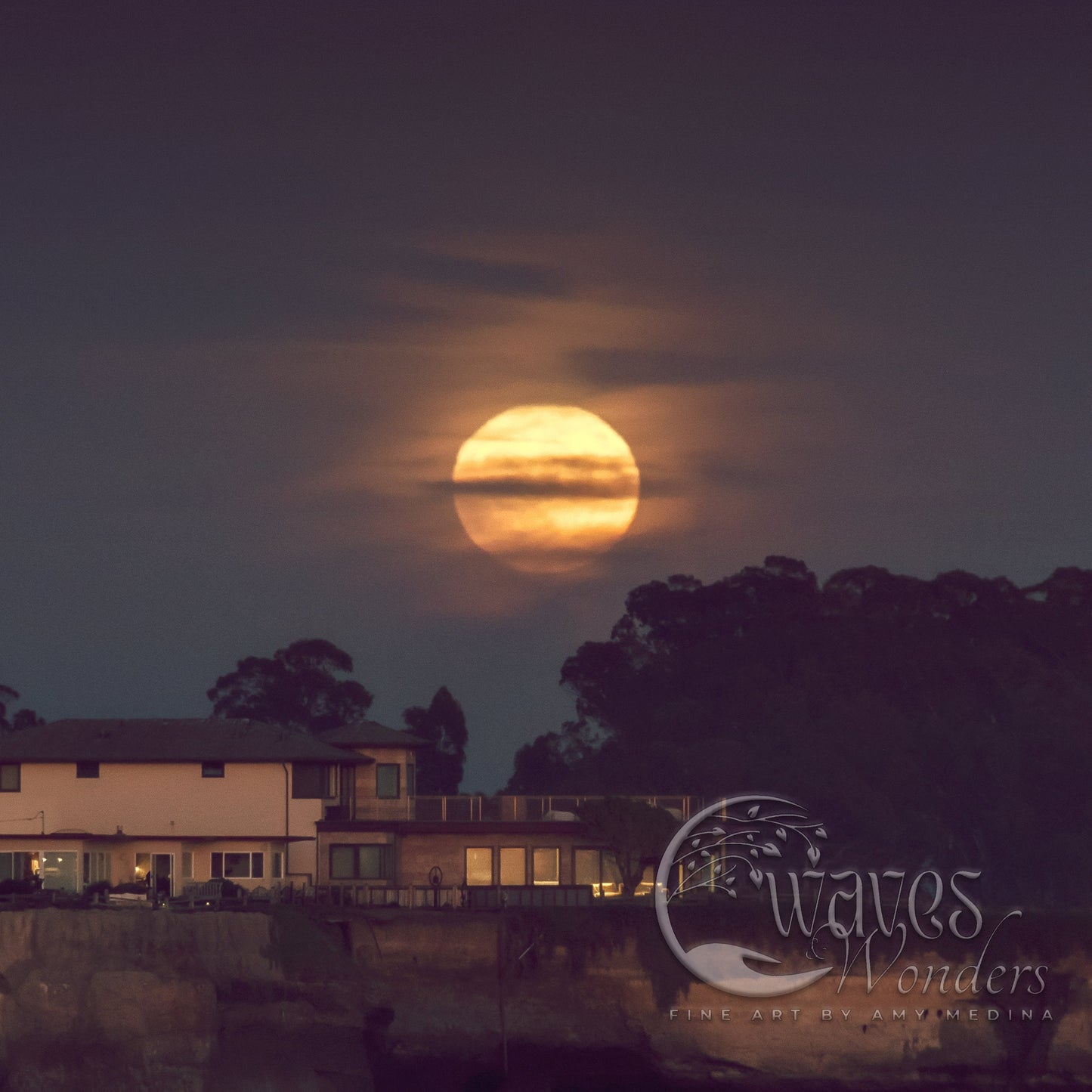 a full moon setting behind a house on a cliff