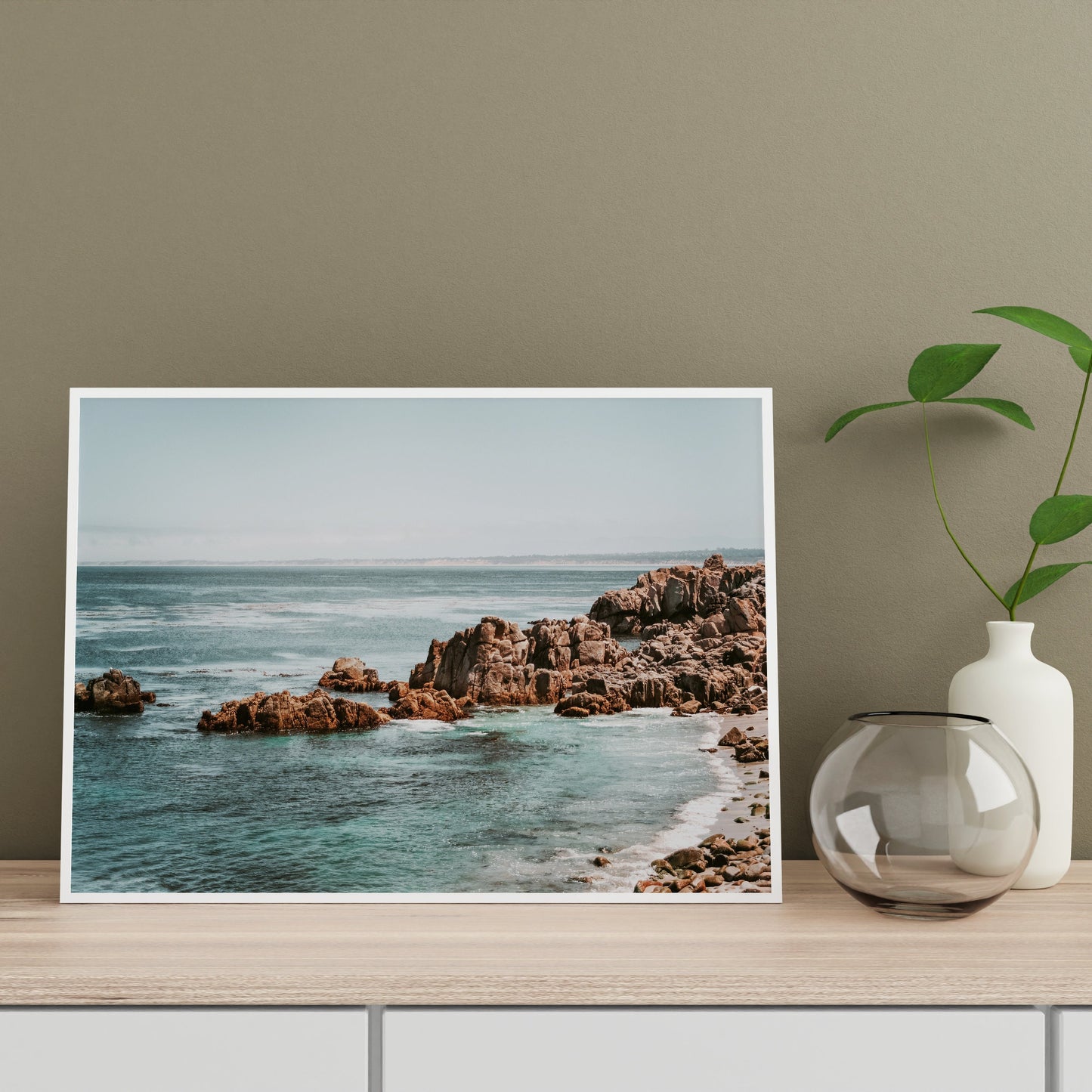 a vase with a plant sits on a shelf next to a photograph of the ocean