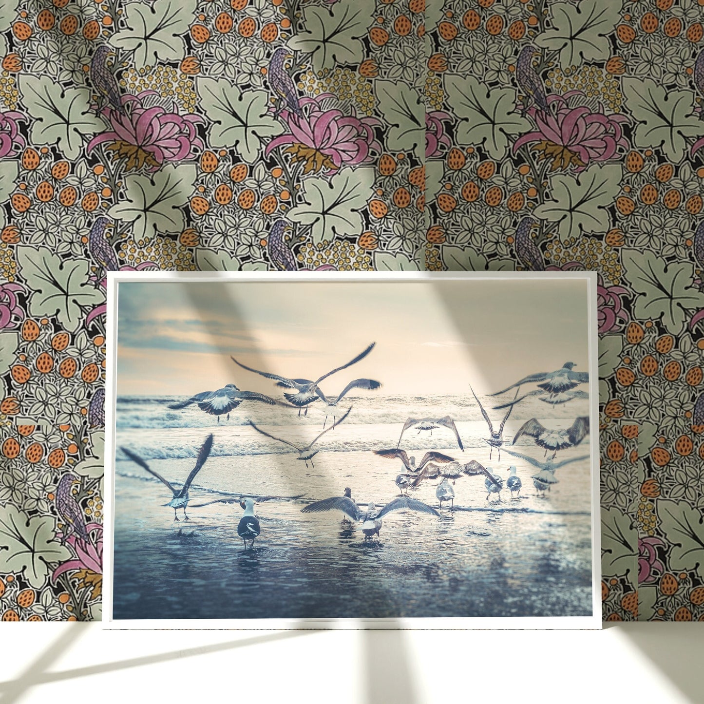 a group of birds flying over a beach next to a wall